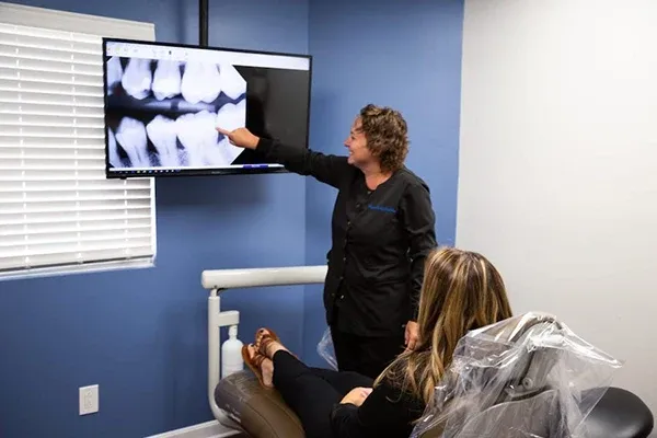 Dental team member pointing at dental X-rays displayed on a large screen while explaining findings to a patient